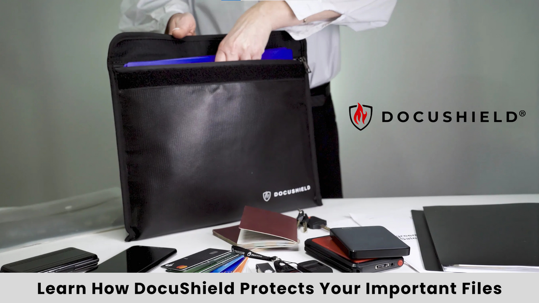 A person placing documents into a black DocuShield fireproof and water-resistant bag, surrounded by passports, electronic devices, and important papers on a desk. The DocuShield logo is visible on the bag, with a tagline emphasizing document security.